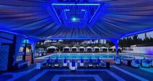 Area lounge all'aperto con illuminazione blu, piscina, gazebo bianchi e pista da ballo in bianco e nero al crepuscolo