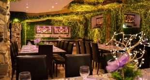 Sala locale Dream Garden Events elegante con pareti verdi, luci decorative dorate, tavoli apparecchiati con tovaglioli lilla e centrotavola floreali