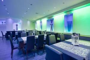 Sala ristorante con tavoli apparecchiati, sedie scure e illuminazione LED verde e blu, con nicchie decorative a parete