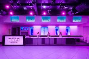Sala eventi J.T. Café con illuminazione viola e rosa, bancone reception illuminato e tavolo decorato con lanterne e fiori