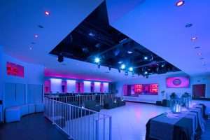 Sala eventi con illuminazione blu e rosa, pista da ballo, area lounge con divani e allestimento tavoli per ricevimento