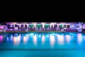 Piscina illuminata di notte con area banchetti all'aperto, luci colorate e parete verde sullo sfondo